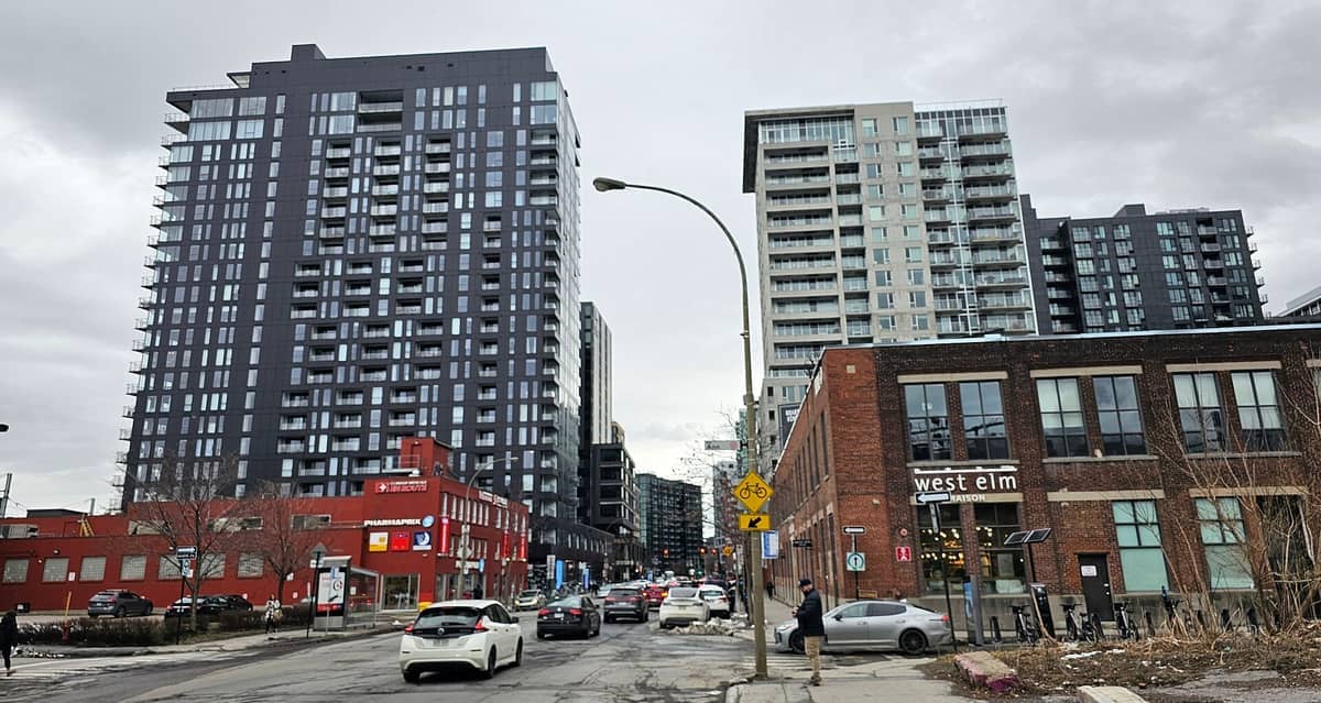 Moderne Hochhaus-Eigentumswohnungen und renovierte Backsteinlagerhäuser säumen eine belebte Straße in Griffintown, Montreal, unter einem bewölkten Winterhimmel.
