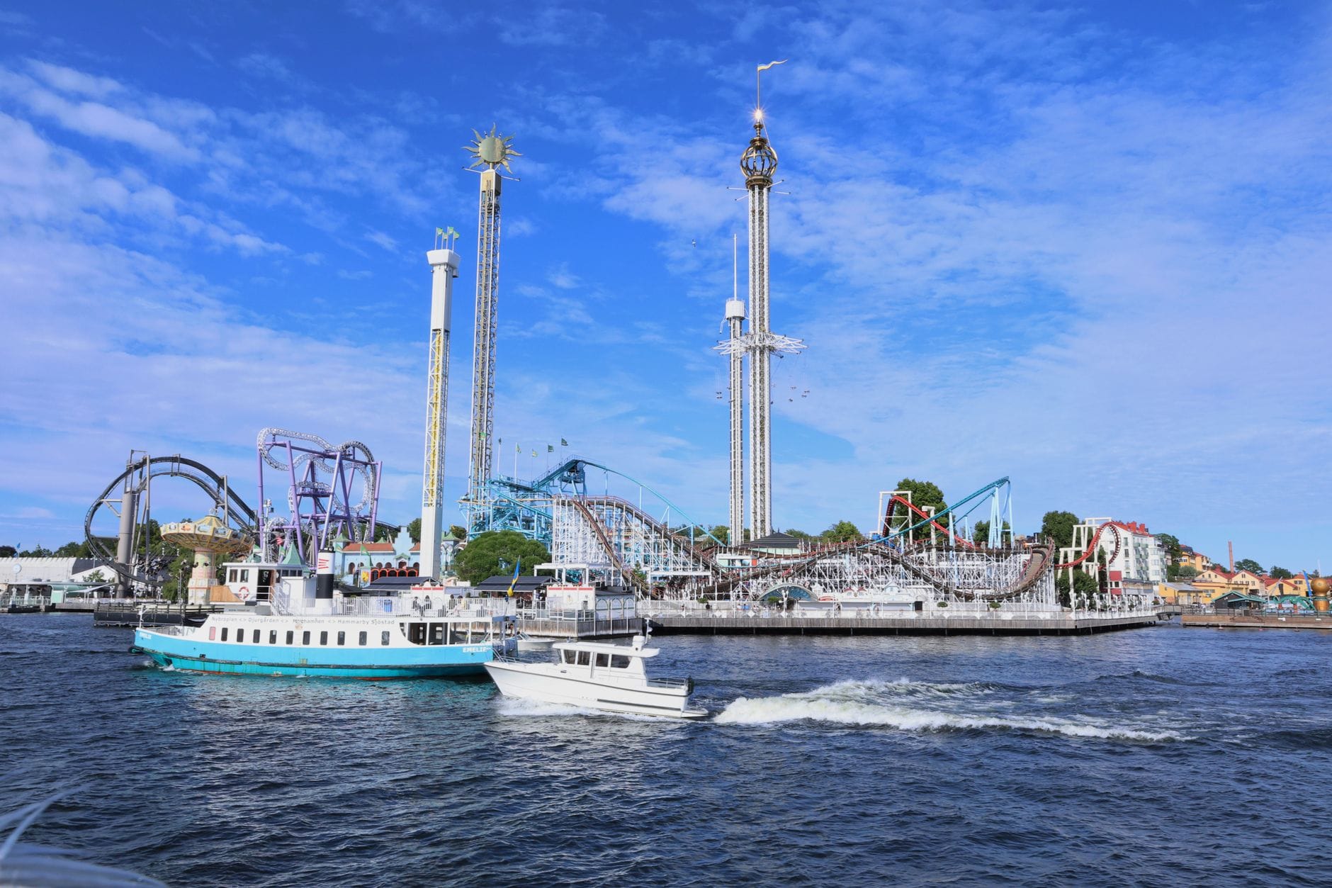 วิวสวนสนุก Gröna Lund จากฝั่งน้ำ เห็นรถไฟเหาะ เครื่องเล่นสูง เรือเฟอรี่ และท้องฟ้าสีฟ้าใส