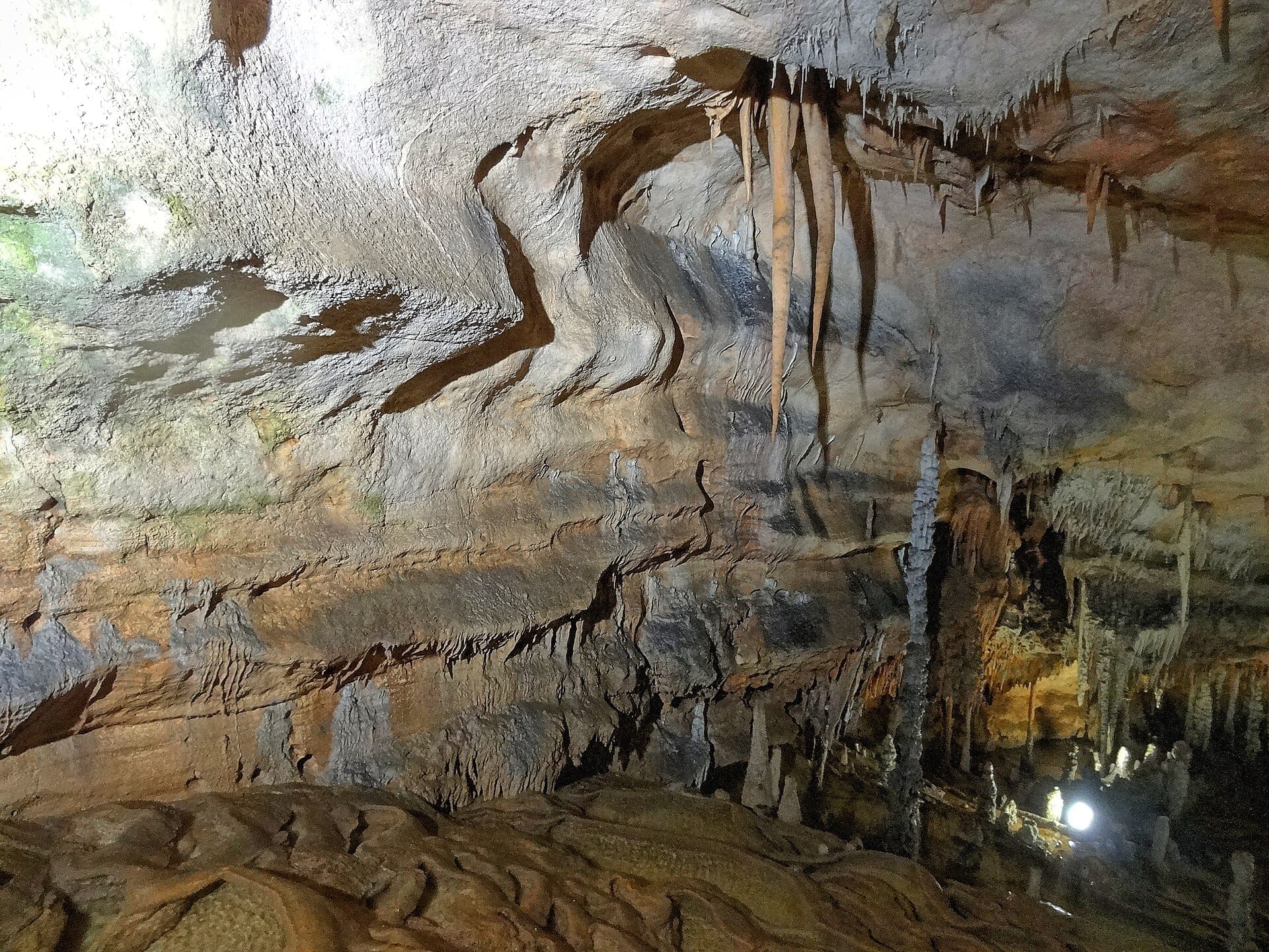 Stalaktiten und strukturierte Kalksteinformationen in der beleuchteten Meereshöhle Grotta del Fico in Baunei, Sardinien, mit erdigen Naturfarben.
