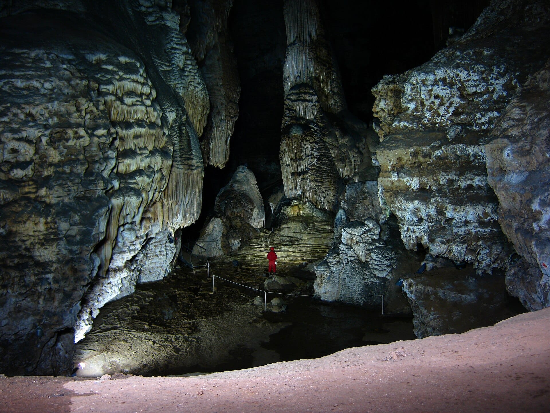 Große Kalksteinkammern, Stalagtitformationen und ein Besucher im roten Anzug in der Grotte Su Marmuri in Ulassai, Sardinien.