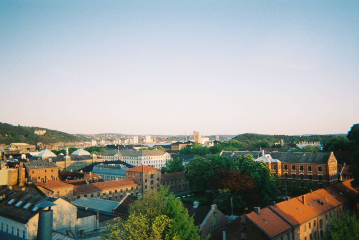 ภาพมุมกว้างของ Grünerløkka กับตึกอุตสาหกรรมเก่า บ้านหลังคาแดง ต้นไม้ร่มรื่น และเส้นขอบฟ้าเมืองออสโลฝั่งเหนือในบรรยากาศชวนเดินเล่น