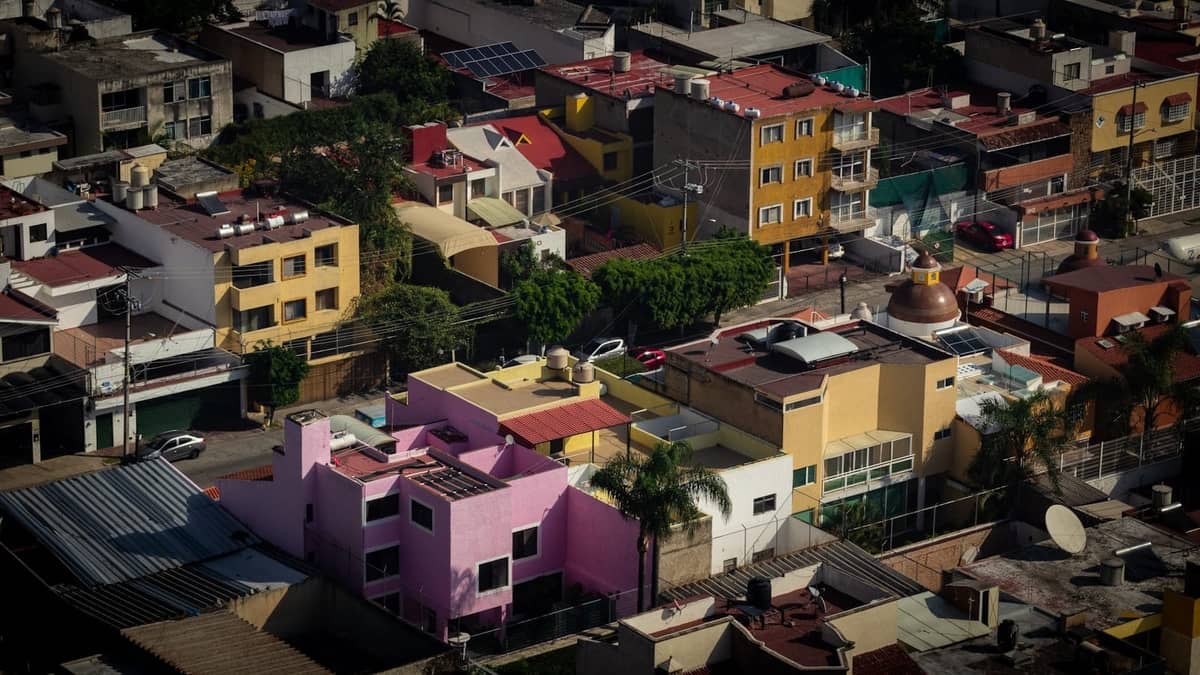 Luftaufnahme eines bunten Wohnviertels in Guadalajara mit verschiedenen Häusern, Grünflächen und städtischem Layout bei Tageslicht.