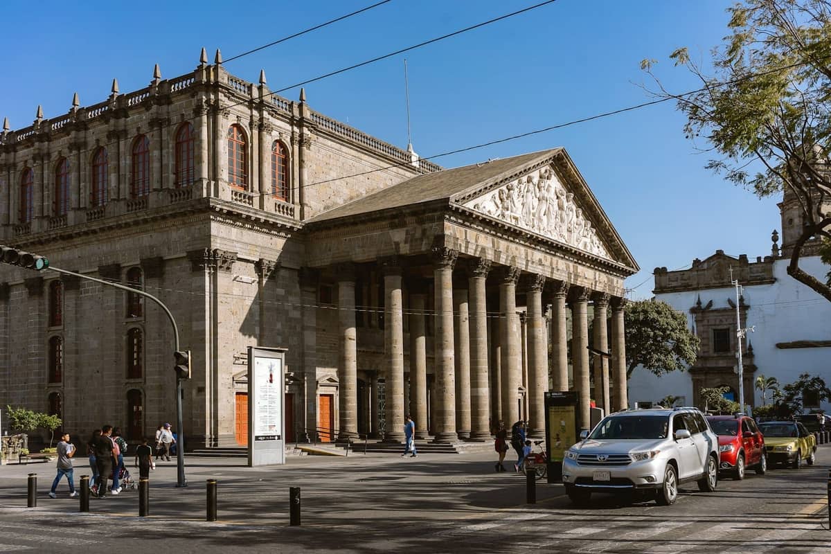 Tagesansicht der neoklassischen Fassade des Teatro Degollado mit korinthischen Säulen, Reliefplastiken und Menschen davor in Guadalajara.