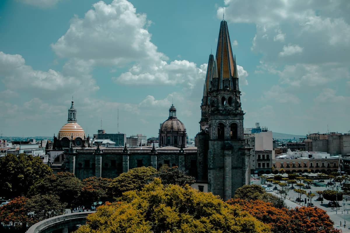 Weitblick auf die Kathedrale von Guadalajara mit ihren markanten Türmen und Kuppeln, die über die umliegenden Bäume und die Stadtlandschaft unter blauem Himmel ragen