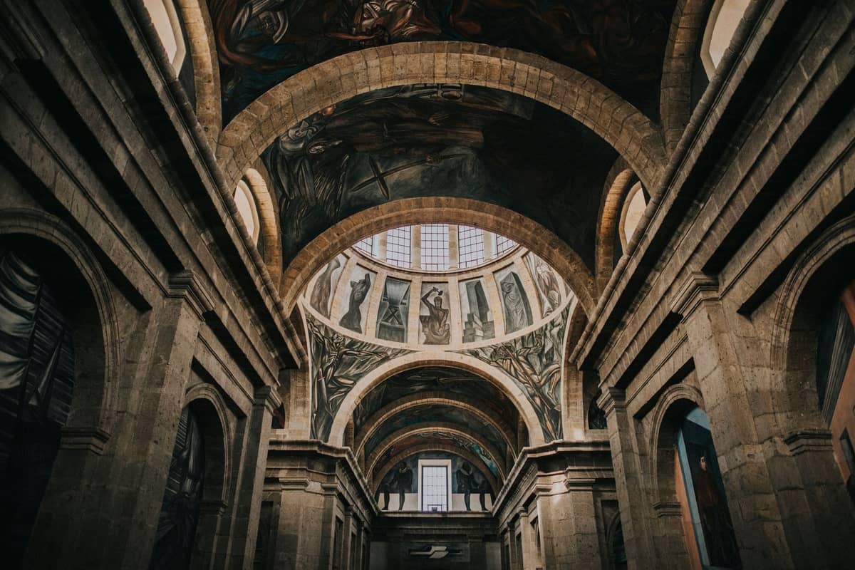 Weitläufige Ansicht des Innenraums des Hospicio Cabañas mit gewölbten Steinhallen und den berühmten Orozco-Wandgemälden unter der Kuppeldecke.