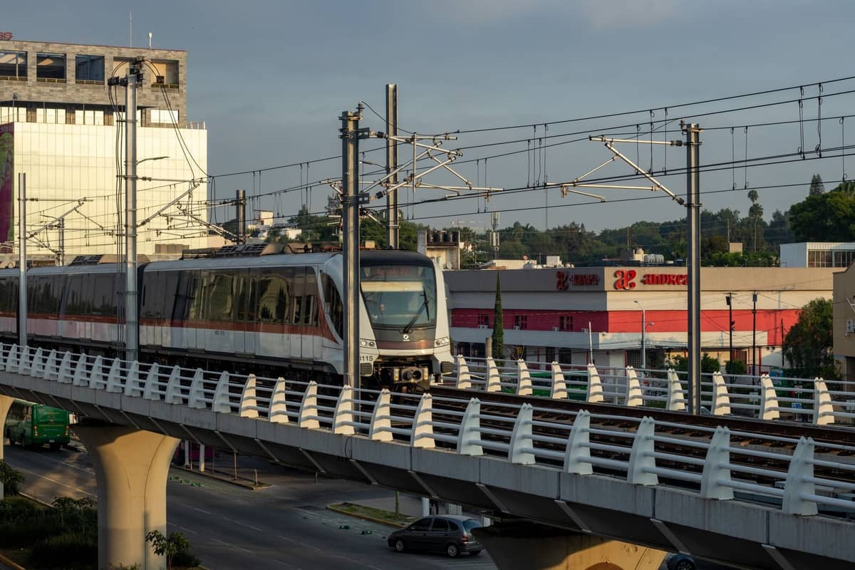 Moderner Stadtbahnzug auf erhöhten Gleisen über einer belebten Straße in Guadalajara, mit Stadtgebäuden im Hintergrund.