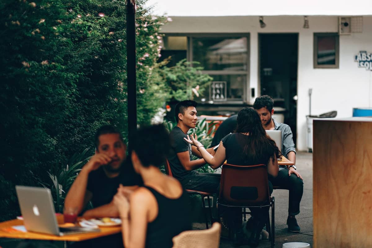 Menschen, die in einem gemütlichen Café im Freien sitzen und sich mit Laptops unterhalten, was auf eine gesellige, digitalnomadenfreundliche Atmosphäre hindeutet.