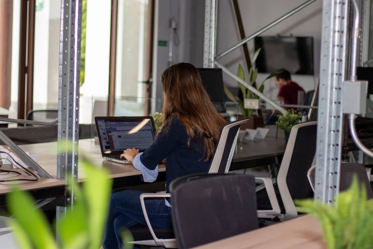 Frau, die in einem modernen Coworking-Space mit Pflanzen und industriellem Dekor an einem Laptop arbeitet, was auf eine produktive Arbeitsumgebung hindeutet.