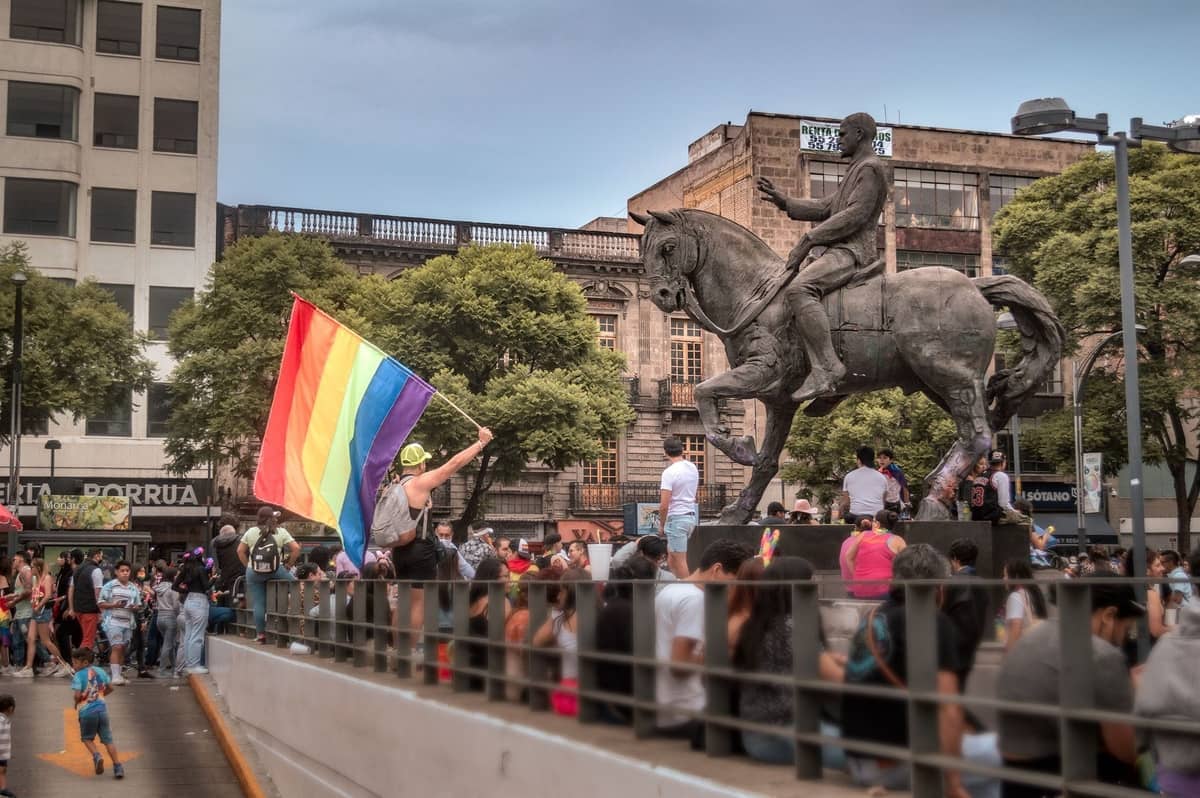 Eine Menschenmenge versammelt sich um das zentrale Reiterstandbild von Guadalajara, während eine Person eine Regenbogenfahne schwenkt und eine lebhafte, bürgerliche Veranstaltungsatmosphäre einfängt.