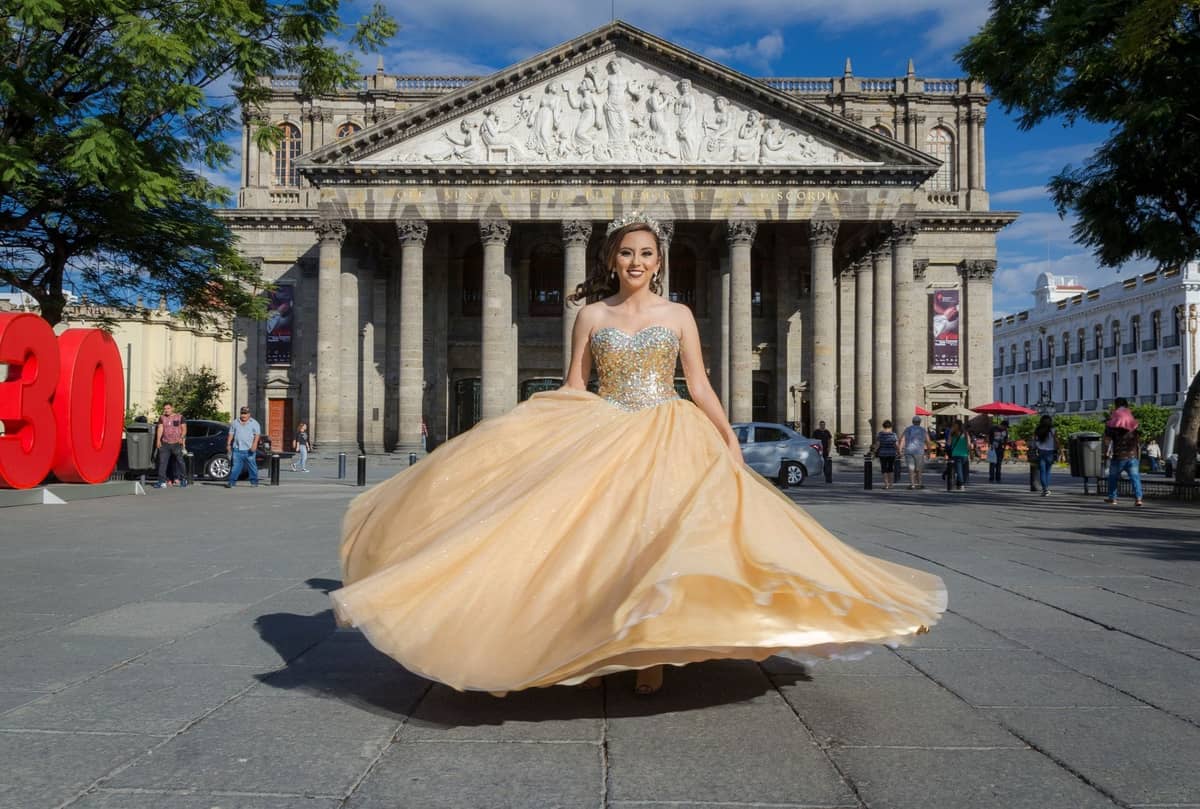 Frau in festlichem Kleid, die sich vor dem bekannten neoklassizistischen Teatro Degollado in Guadalajara dreht, mit Menschen und Bannern auf dem Platz.
