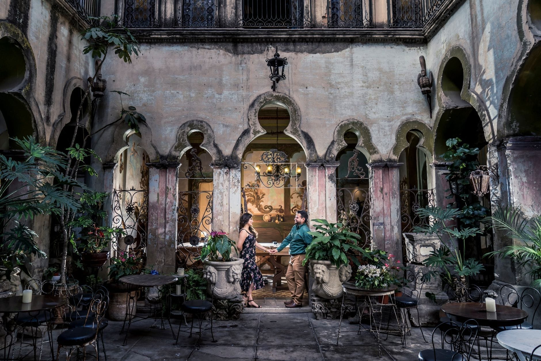 Um casal romântico no centro de um café histórico e exuberante, com arcos, detalhes ornamentados e atmosfera intimista em Guadalajara.