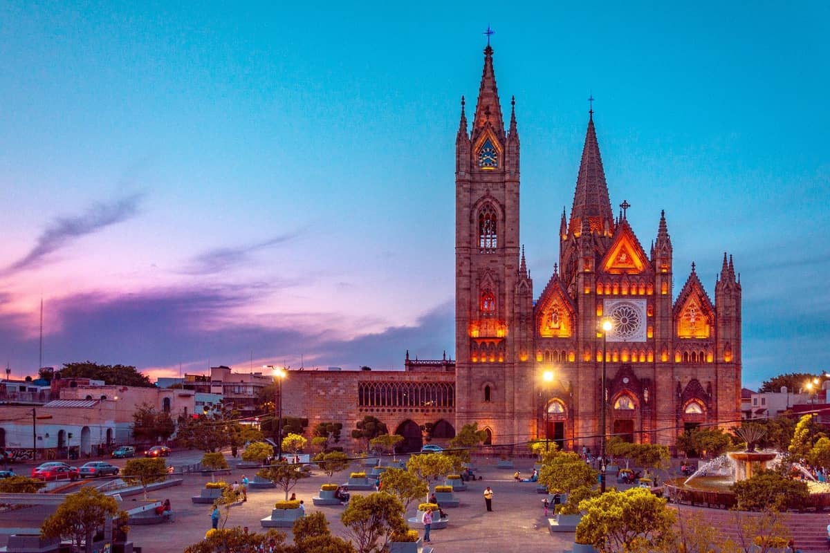 Abenddämmerung mit beleuchtetem Templo Expiatorio und weitläufigem Platz, mit Bäumen und Paaren, die im romantischen Abendlicht spazieren.