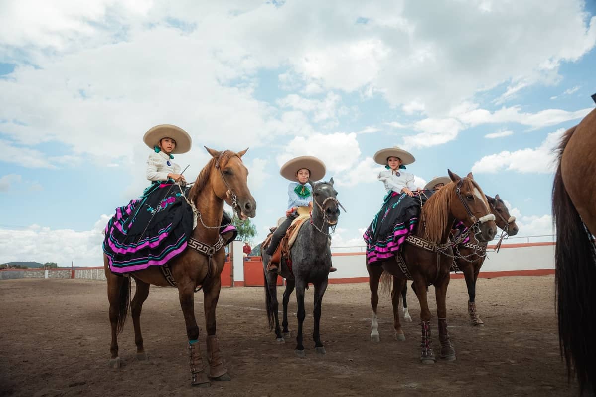 Frauen in traditioneller Escaramuza-Rodeotracht zu Pferd in einer Arena unter strahlend blauem Himmel, die die Charrería-Kultur in Mexiko festhalten.