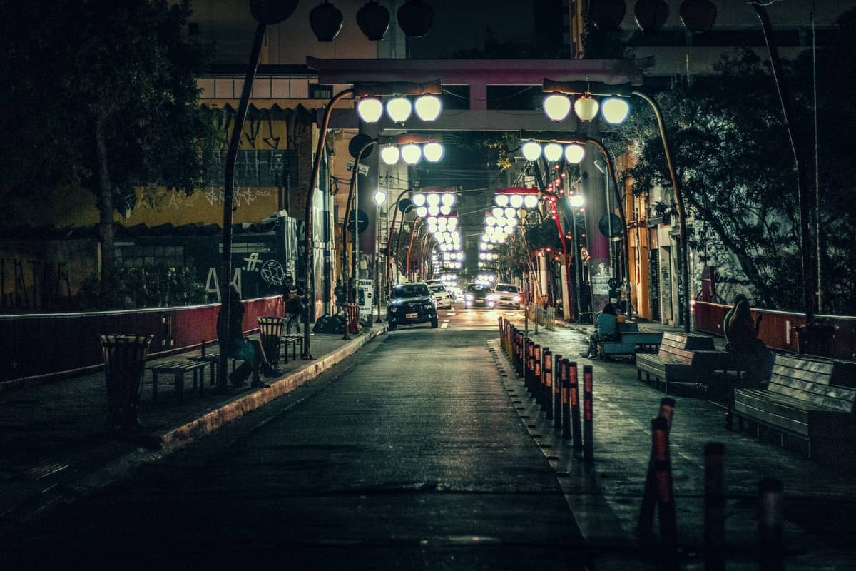 Nachtansicht einer beleuchteten Fußgängerbrücke in einem urbanen Nachtlebenviertel von Guadalajara, mit Straßenlaternen und Menschen auf Bänken.