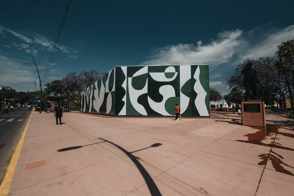 Weitläufiger Platz in Guadalajara mit einem markanten modernen Gebäude und öffentlicher Kunst unter blauem Himmel, Menschen spazieren draußen, die lokale Atmosphäre widerspiegelnd.