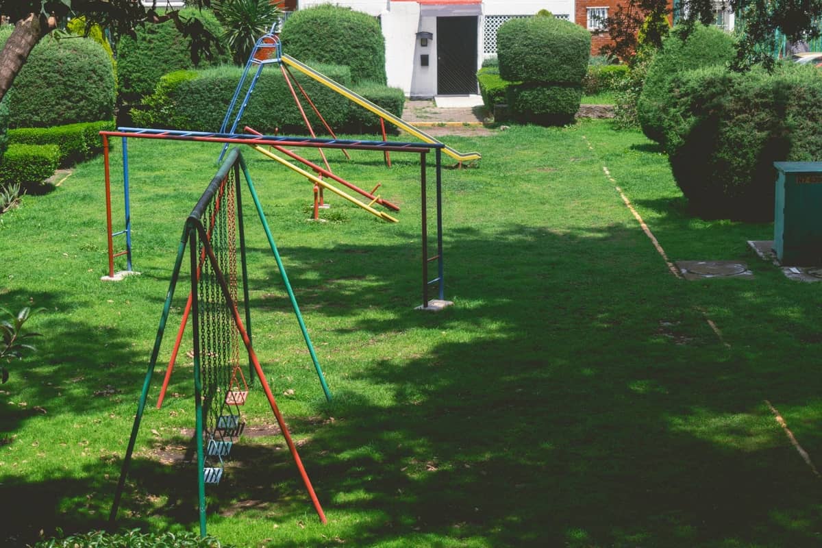 Ein grüner Stadtteilpark in Guadalajara mit bunten Spielgeräten, Rutschen und gestutzten Büschen unter sonnigem Himmel.