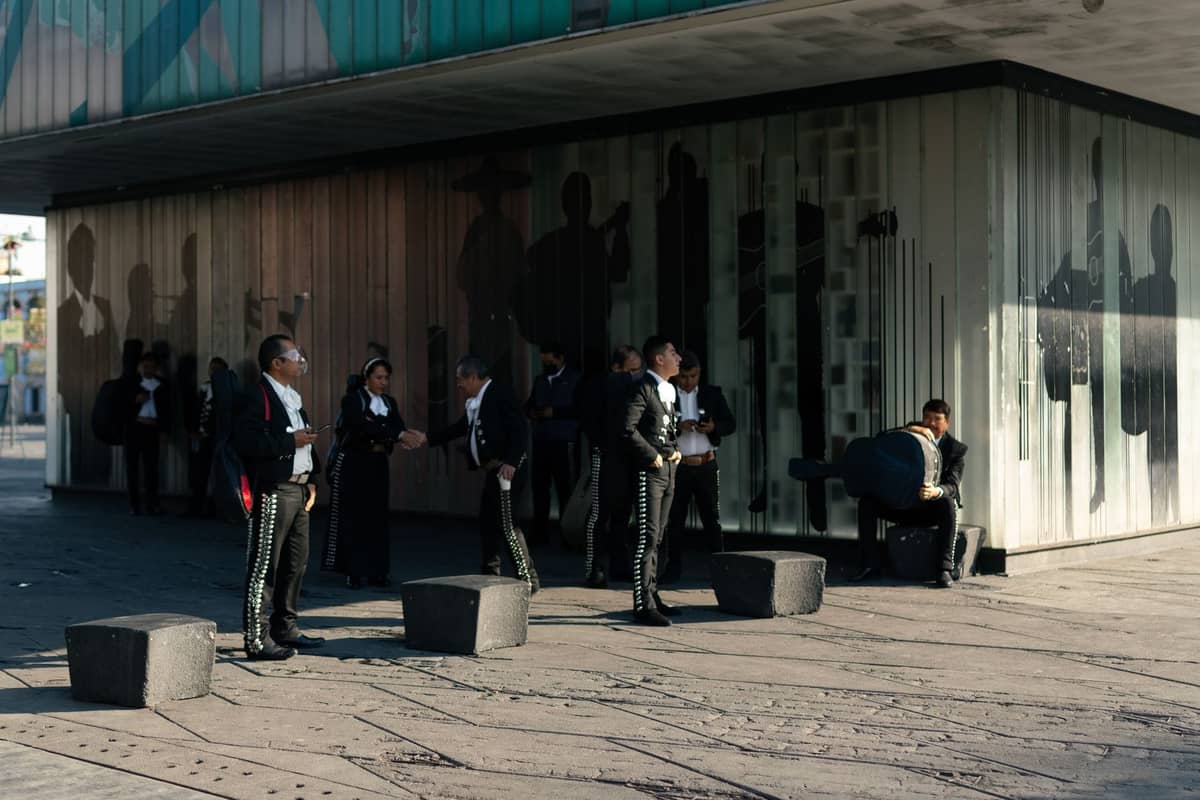 Mehrere Mariachi-Musiker in vollständiger traditioneller Tracht vor einem modernen Gebäude mit künstlerischem Wandgemälde, die die kulturelle Atmosphäre von Guadalajara widerspiegeln.