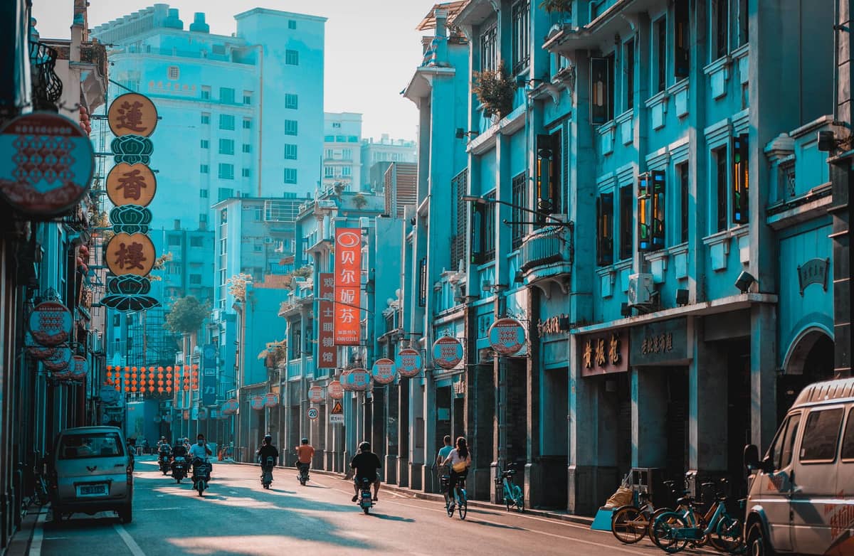 Vista da rua dos edifícios de arcada qilou em Guangzhou, com andares superiores em balanço e passagens cobertas, ladeados por lojas e letreiros chineses coloridos.