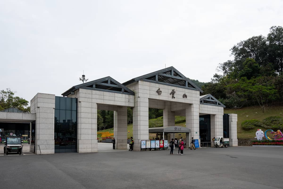 Portão principal da Montanha Baiyun em Guangzhou, com o nome em caracteres chineses e visitantes entrando na área do parque.