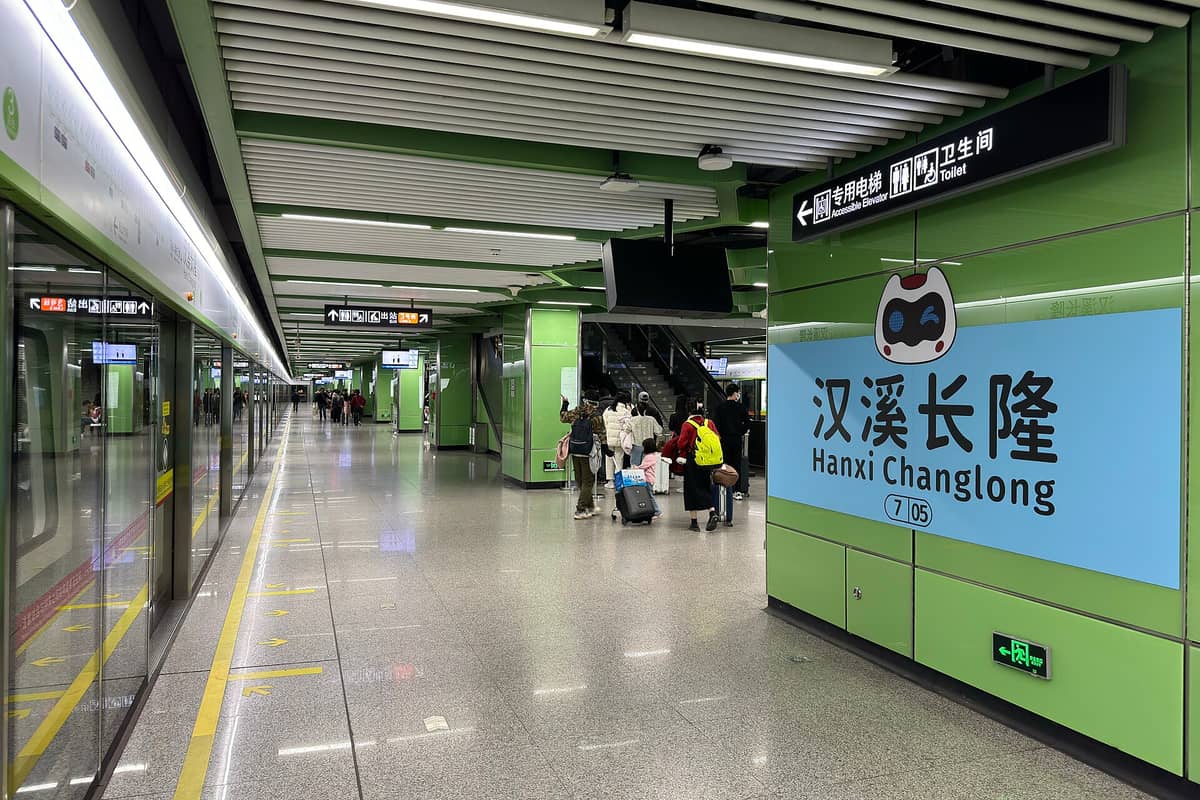 Wide view of Hanxi Changlong metro station interior in Guangzhou, showing the platform, clear station signage, and passengers with luggage.