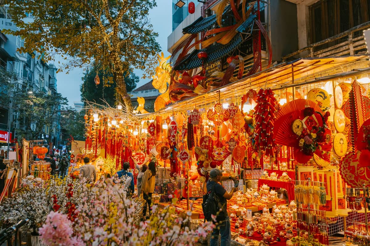 Bustling Guangzhou street market with Chinese New Year decorations, lanterns, and crowds shopping among bright festive stalls in the evening.