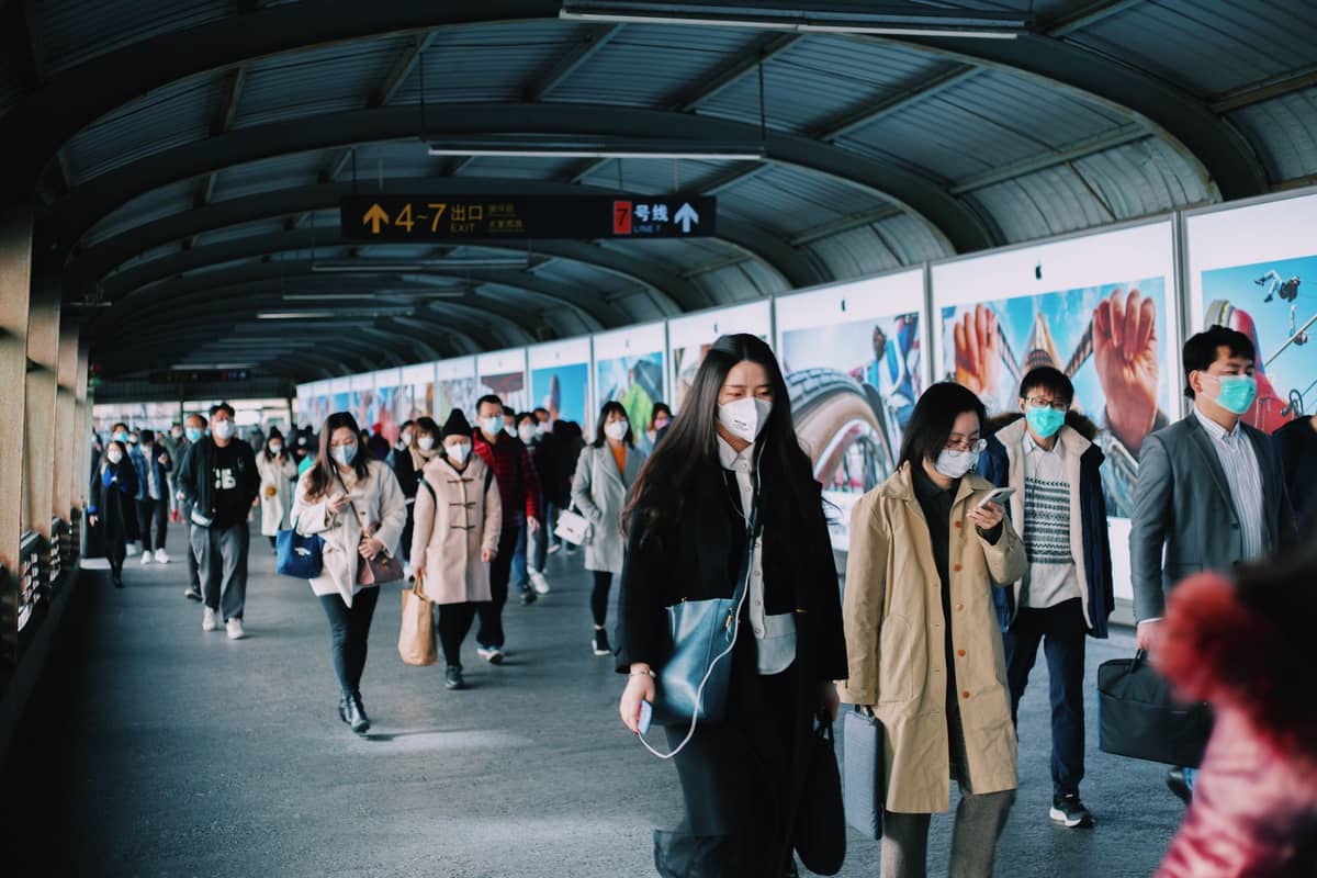 Crowds of people with luggage walk through a busy, covered pedestrian walkway in a Chinese transit hub.
