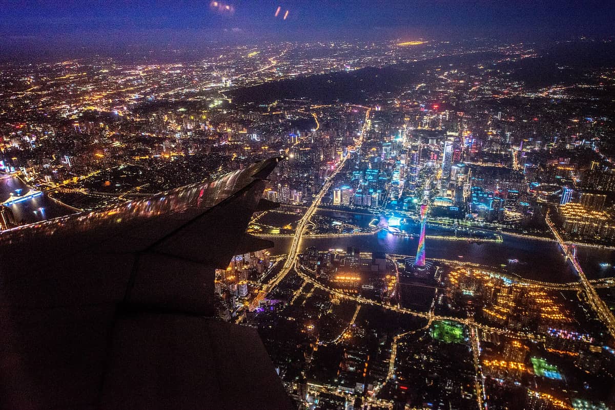 Aerial night view of Guangzhou with airplane wing, city lights, Pearl River, and Canton Tower in the distance.