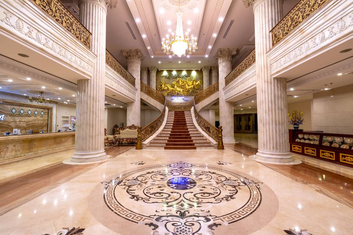 Grand hotel lobby with ornate columns, a sweeping staircase, chandelier and marble floor in luxury style.