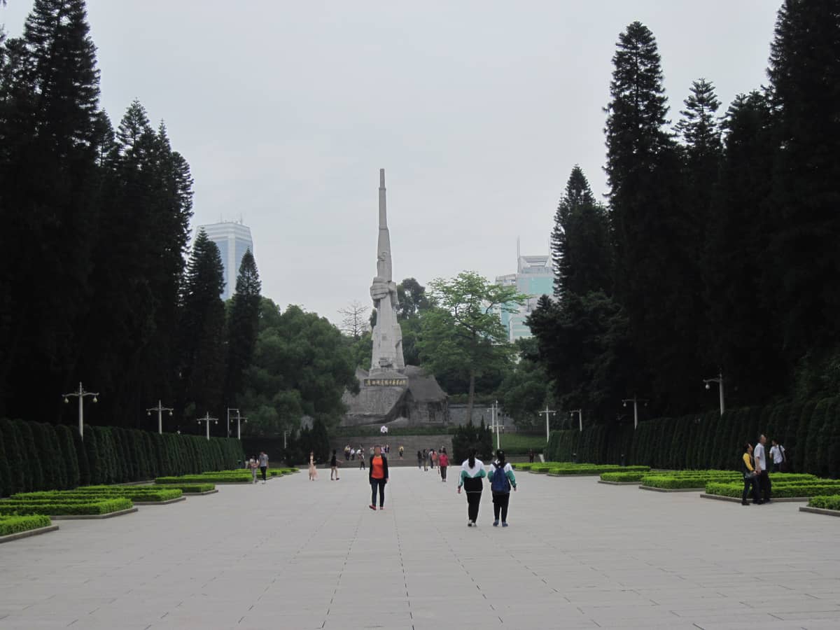 Central walkway in Guangzhou Martyrs' Memorial Garden, lined with tall trees and leading to the large memorial monument in the distance.