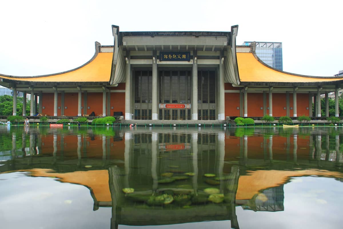 Modern building with distinctive yellow-tiled roof reflected in a pond, likely a famous memorial or political history site in Guangzhou.
