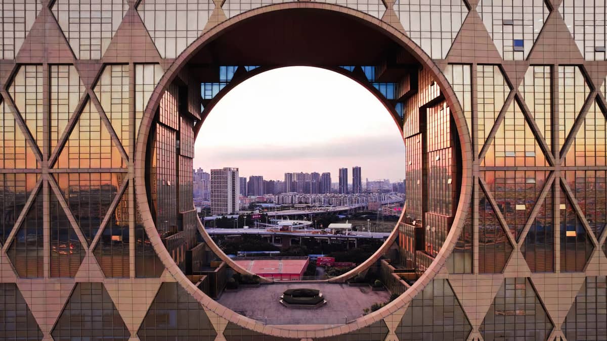 Striking circular window in the facade of Guangzhou's iconic Guangzhou Circle, with cityscape visible through the geometric architecture at sunset.