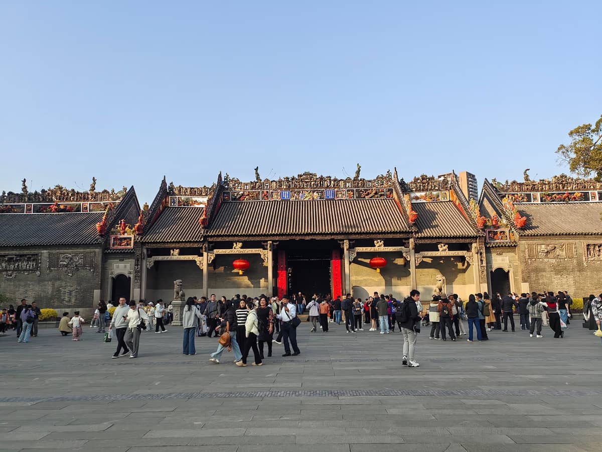 Wide view of the ornate roof and entrance of the Chen Clan Ancestral Hall, with crowds of visitors in the plaza on a sunny day.