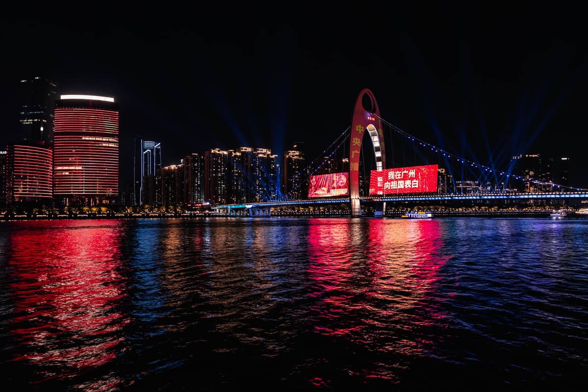Night view of Guangzhou’s iconic Liede Bridge and riverside skyscrapers brightly lit with colorful reflections on the Pearl River, capturing the city’s lively after-dark atmosphere.