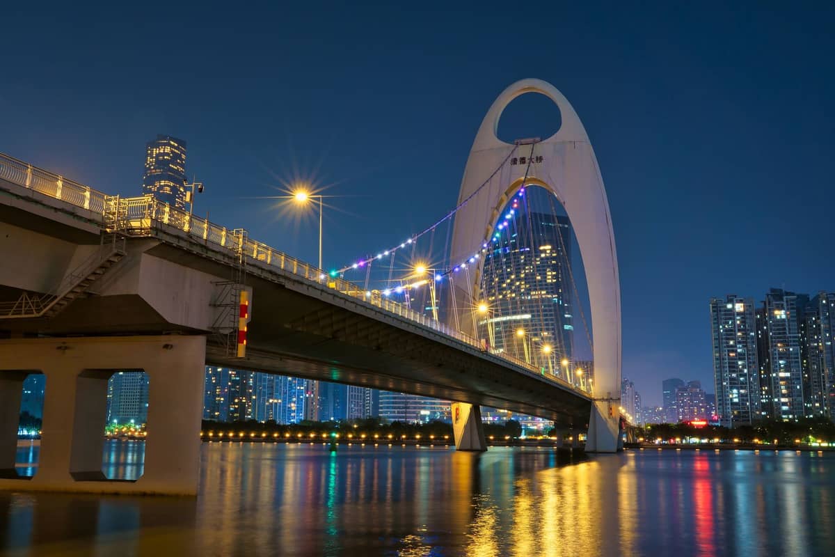 Night view of Guangzhou's iconic Liede Bridge over the Pearl River, city skyline illuminated, and reflections shimmering in the water.