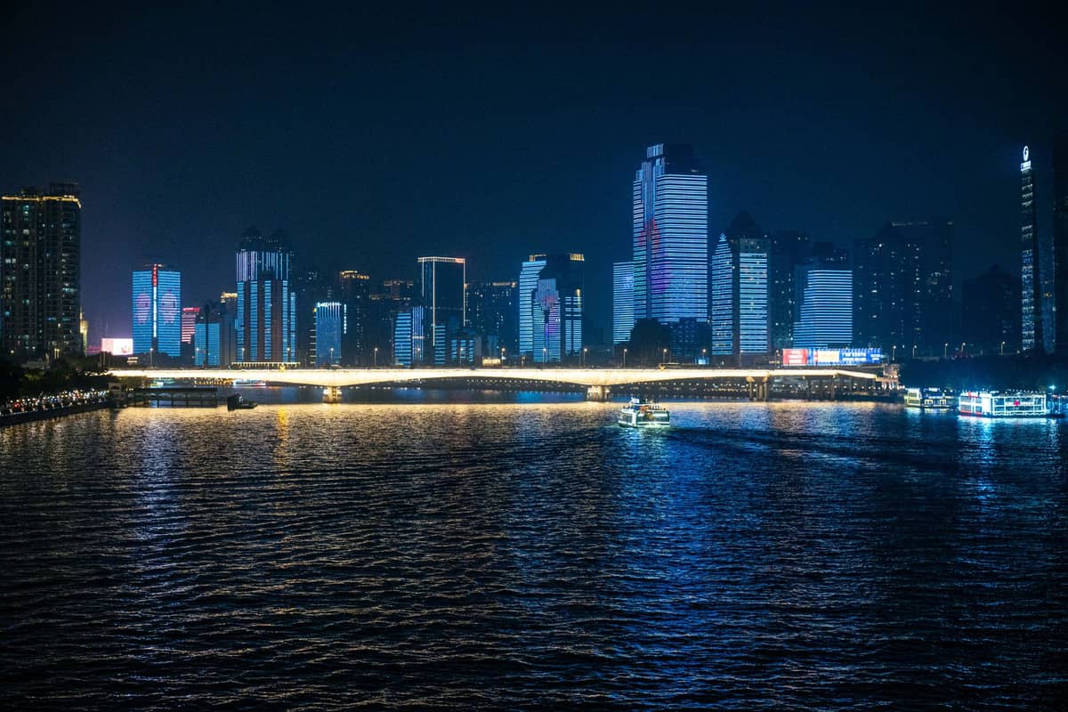Night view of a modern skyline along a wide river in Guangzhou, with illuminated skyscrapers and reflections on the water.