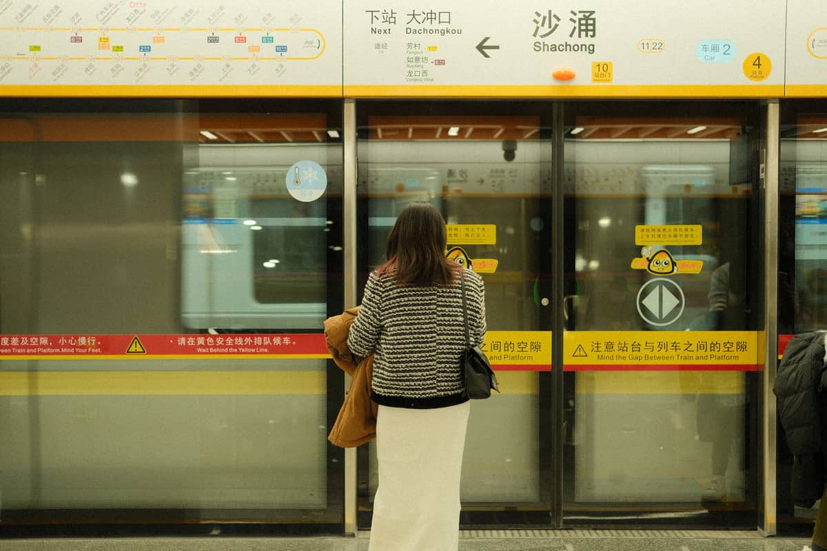 Person standing in front of closed subway platform doors with metro map and station signs in Chinese above.