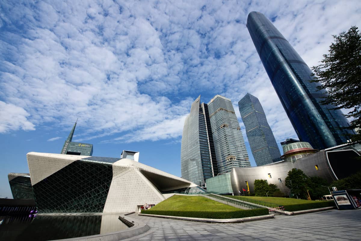 Wide angle view of the Guangzhou Opera House’s distinctive river-stone shaped exterior with surrounding skyscrapers and blue sky in Zhujiang New Town.