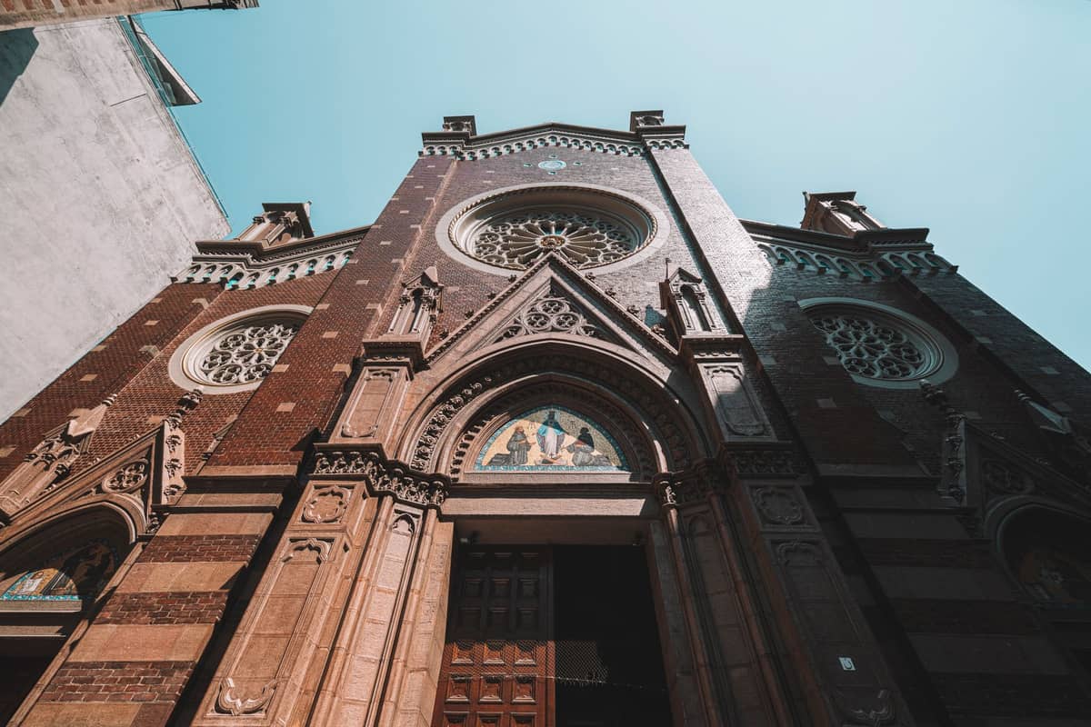 Facade of a large Gothic-style church with a rose window, religious statues, and intricate brick details under a clear sky.