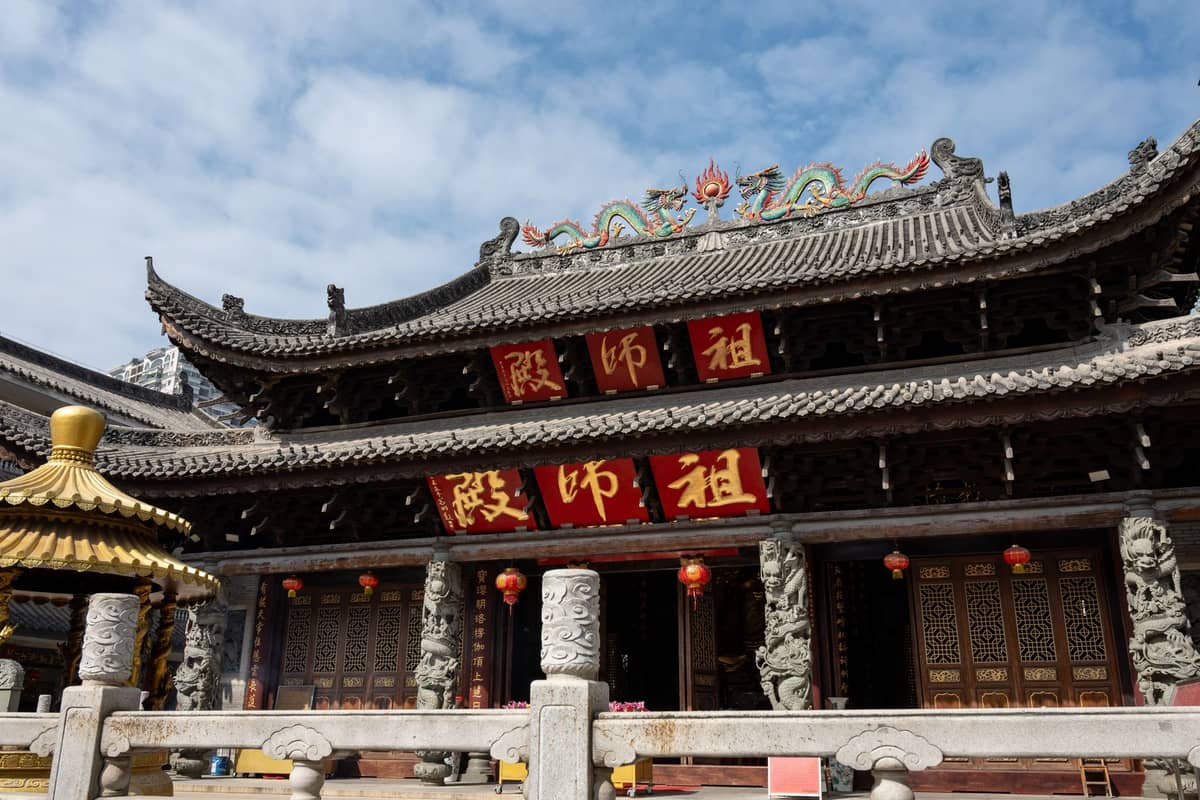 Front view of a traditional Chinese temple in Guangzhou with intricate roof decorations, red columns, gold characters, and stone carvings at the entrance.