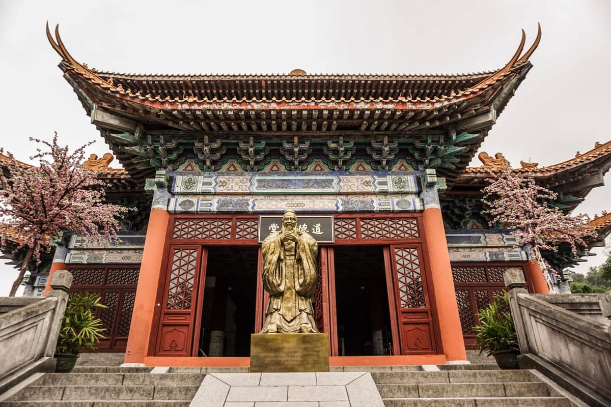 Ornate Taoist temple entrance with a golden deity statue, traditional roof, red columns, and blossoming trees in front, ideal for Guangzhou folk religion sites.
