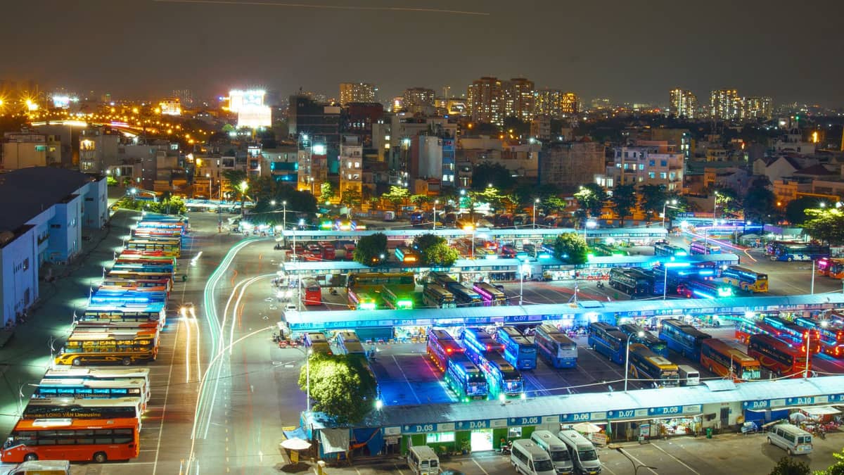 A large Guangzhou bus terminal at night, filled with many coaches and buses lined up under bright lights, with the city skyline in the background.
