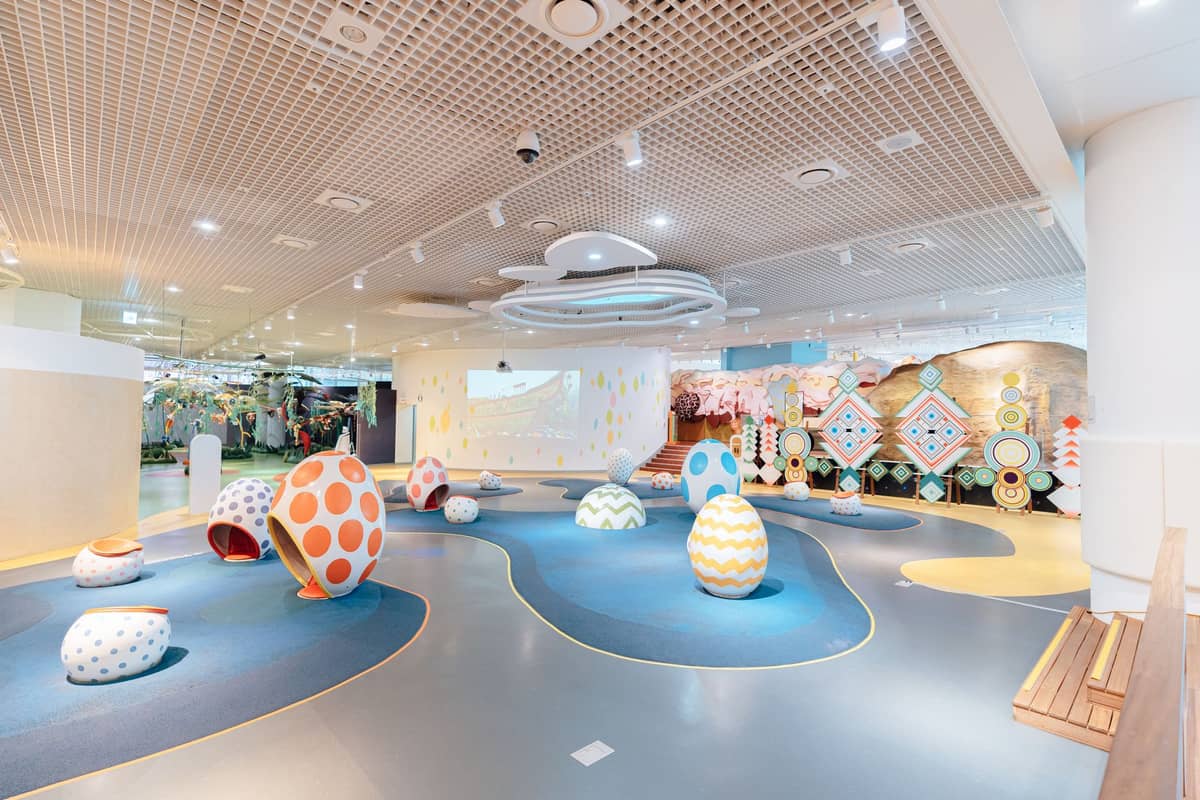 Colorful indoor children's playground with large egg-shaped decorations, soft play surfaces, and whimsical decor under bright lighting.