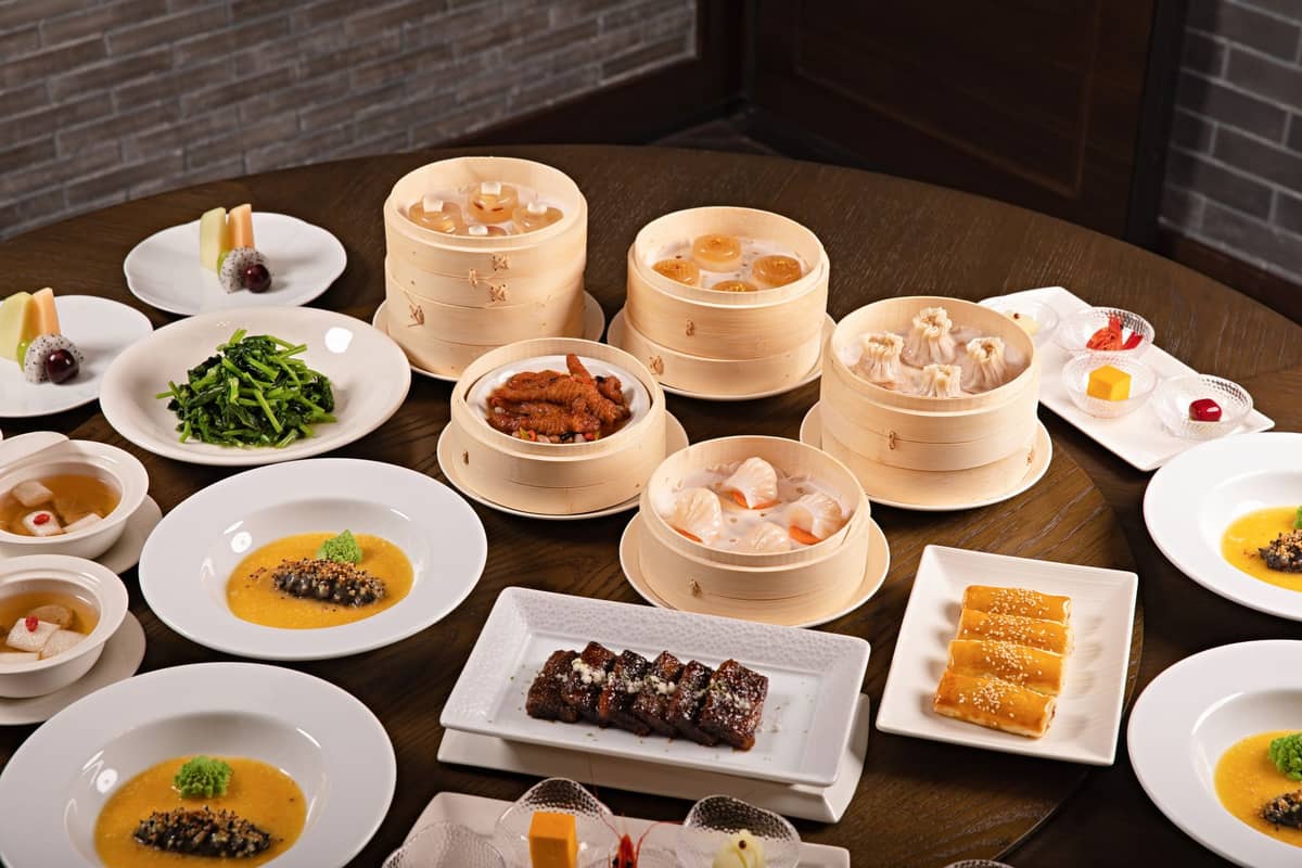 A table filled with Cantonese dim sum, bamboo steamers, small plates of food and desserts, capturing a classic yum cha meal.