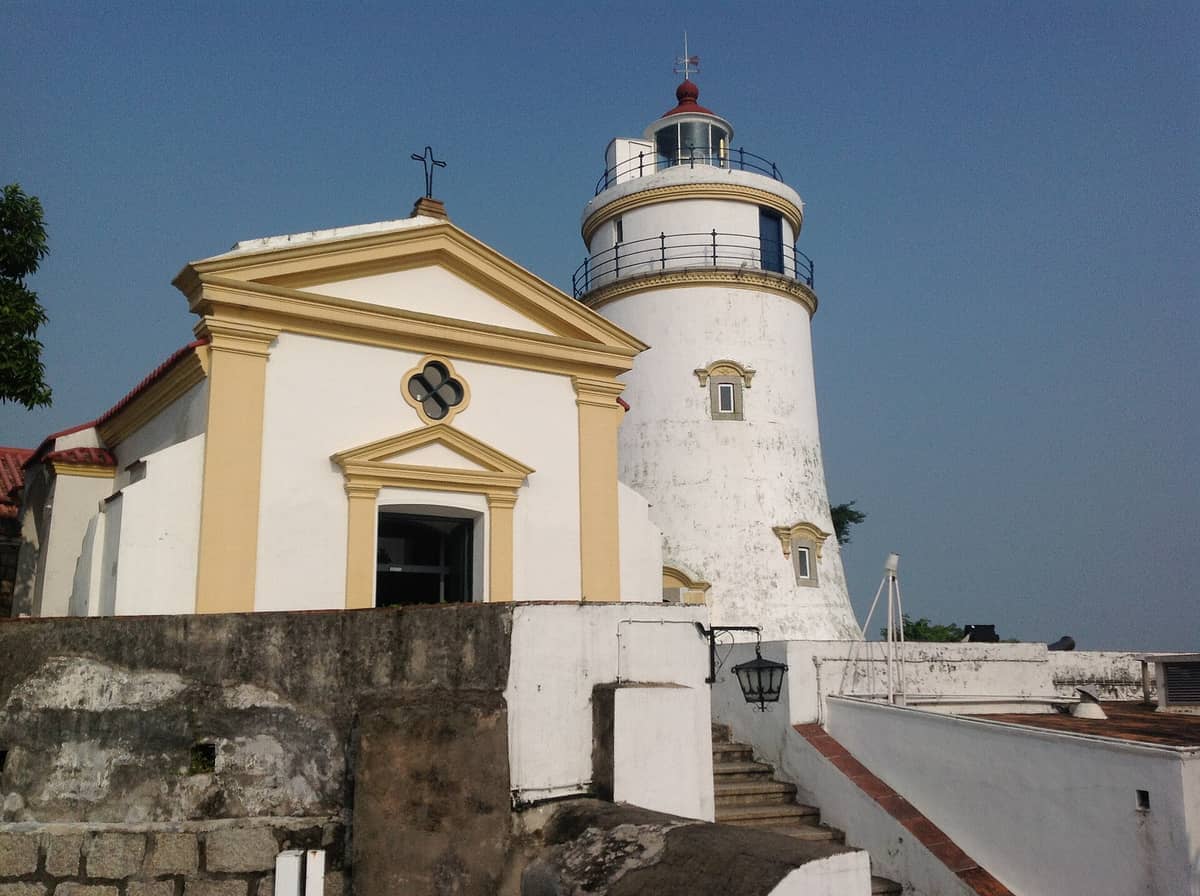 Festung und Leuchtturm Guia in Macau, mit dem historischen weißen Turm und der Kapelle mit gelben Verzierungen an einem klaren Tag.