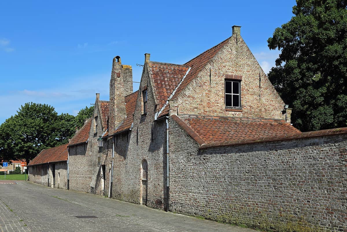 Historic brick facade of the Guido Gezelle Museum in Bruges, featuring sloped roofs and chimneys under a bright blue sky.
