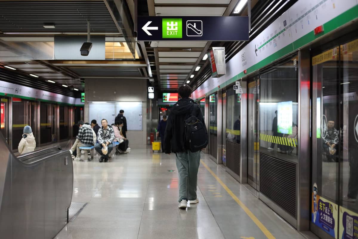 Plataforma da estação de metrô de Seul com passageiros, sinalização de SAÍDA clara e portas de segurança de vidro, ilustrando o acesso ao transporte público.