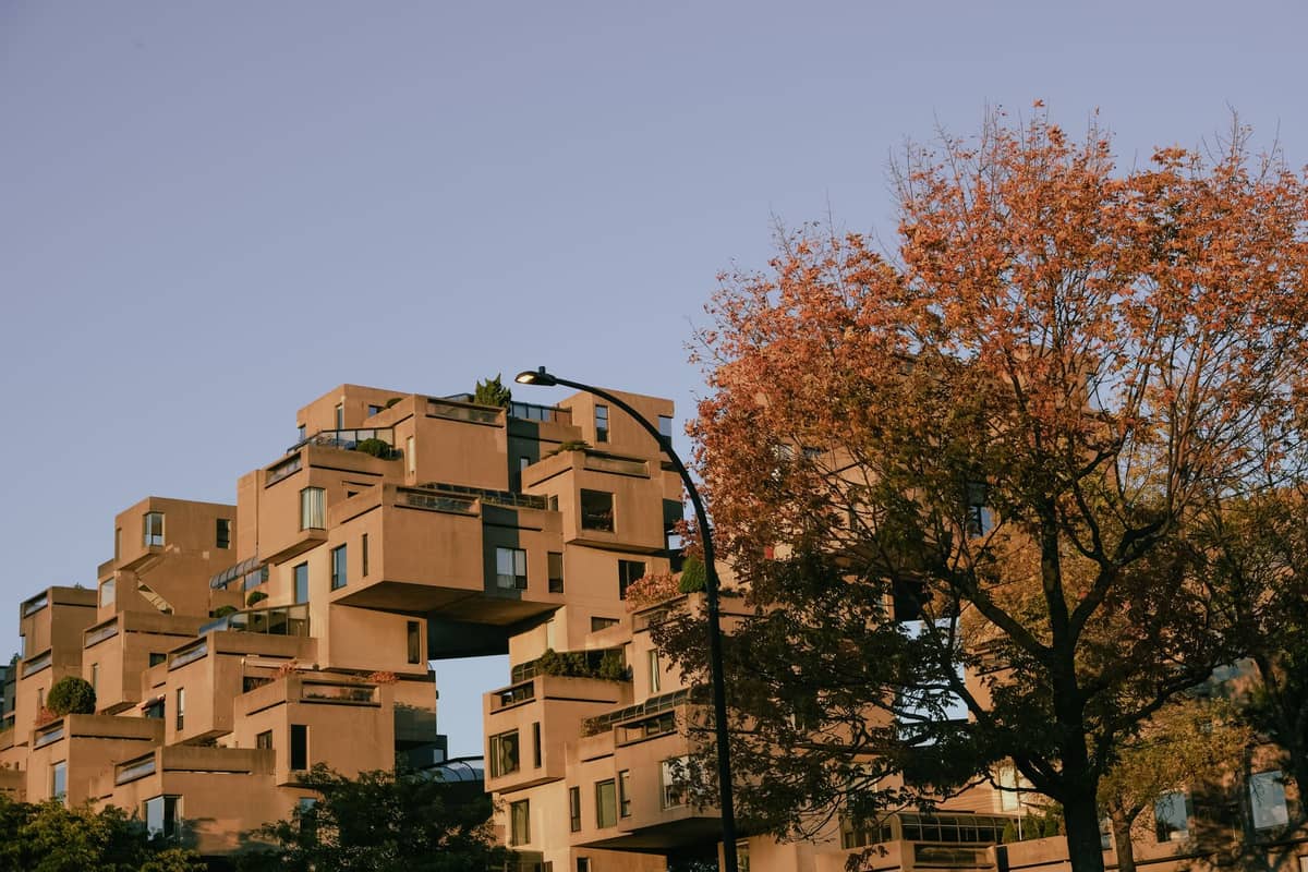 Weitwinkelpanorama der gestapelten Betonwürfel von Habitat 67 mit einem Baum in Herbstfärbung und strahlend blauem Himmel über Montréal.