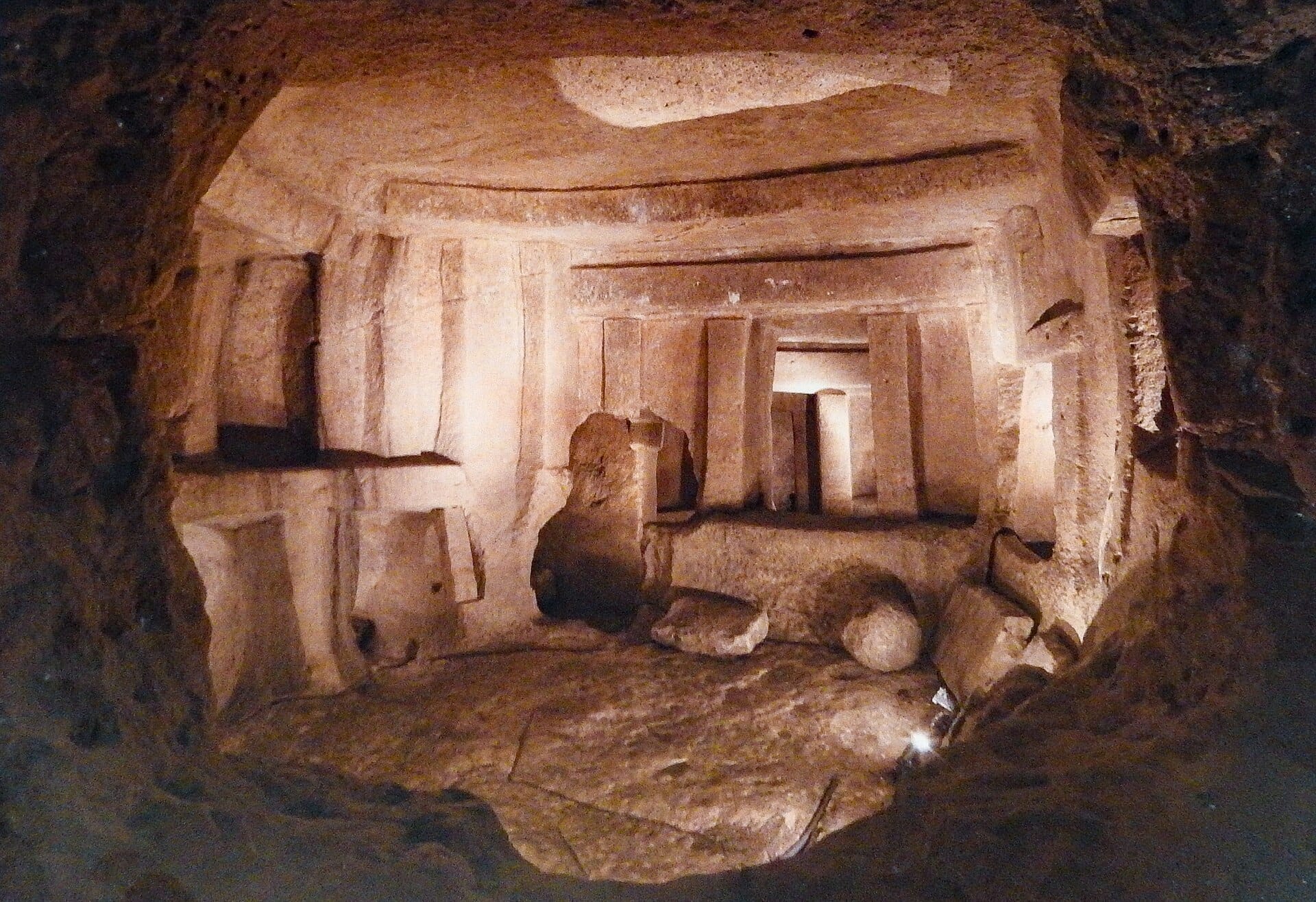 Camera interna in pietra dei templi di Ħaġar Qim, con grandi megaliti, pareti scolpite e illuminazione ambientale soffusa.
