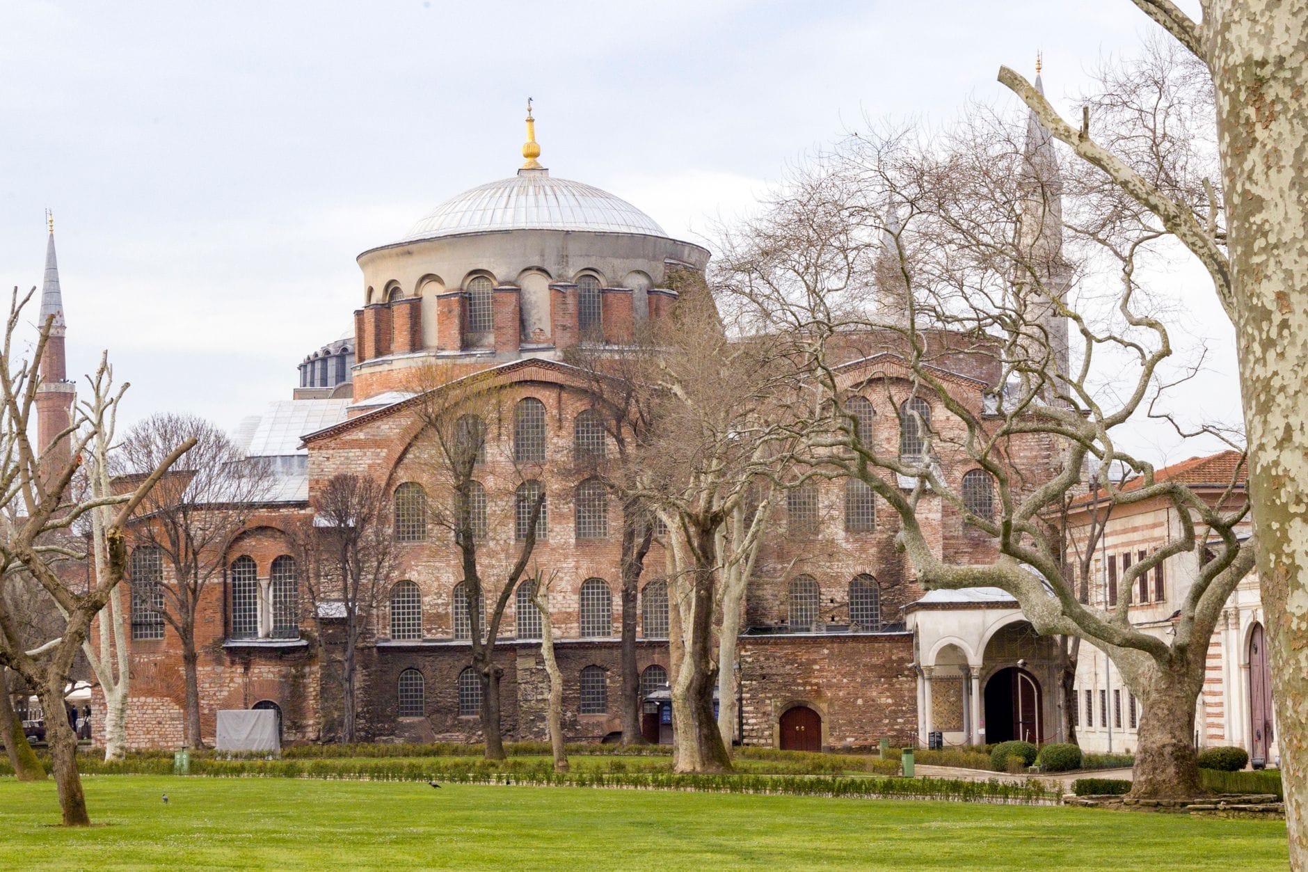 Vista panoramica dell'esterno del Museo Hagia Irene con la sua caratteristica cupola, i mattoni a vista, le finestre ad arco e gli alberi spogli nei giardini del Palazzo di Topkapı.