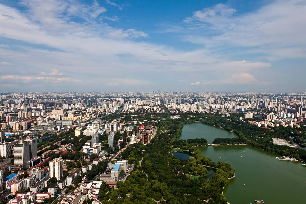 Luftaufnahme des Bezirks Haidian in Peking mit üppig grünen Parks, großen Seen und weitläufiger Stadtbebauung unter blauem Himmel.